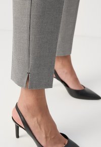 Pantalons chevilles à carreaux noir et blanc avec des fentes latérales, associés à des talons noirs pointus. Tissu lisse avec une coupe structurée.