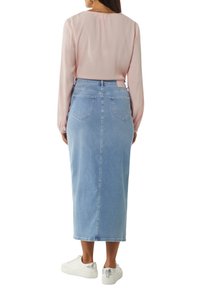Lichtroze blouse met lange mouwen, gecombineerd met een denim midi-rok. De rok is lichtblauw met twee achterzakken en een getailleerde taille. Witte sneakers maken de look af.