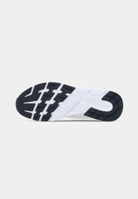 Sole of a white sneaker with black tread, showing deep grooves for traction and the brand name embossed near the heel.