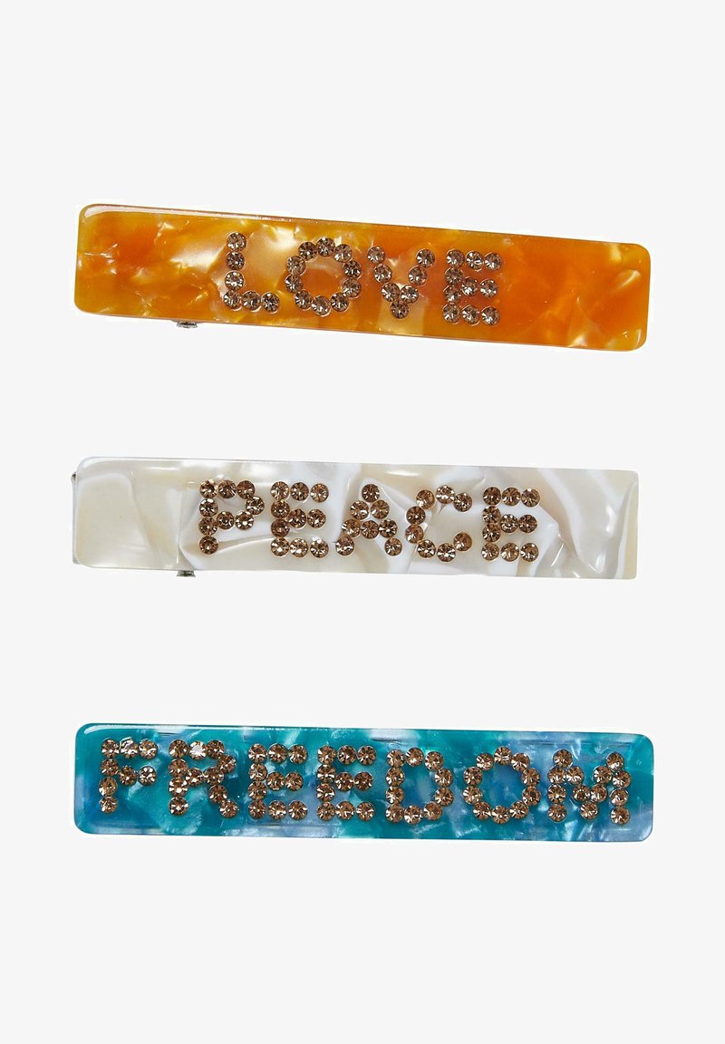 Three hair clips: orange with "LOVE" in rhinestones, white with "PEACE," and aqua with "FREEDOM," all featuring a marbled finish.