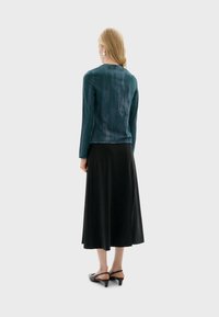 T-shirt met lange mouwen in teal met subtiele textuur, gecombineerd met een zwarte, vloeiende rok en grijze schoenen met hakken, gezien van achteren.