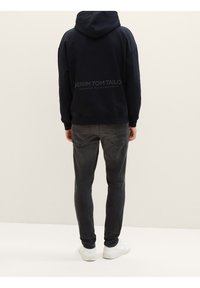 Námořnická mikina s kapucí a logem na zádech, spárovaná se šedými slim-fit džíny a bílými teniskami. Směs bavlny, uvolněný střih.