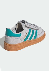 Baskets en daim gris avec des rayures turquoise, semelle en caoutchouc gomme, col rembourré et accents texturés. Présente un marquage doré sur le côté.