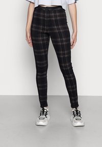 Pantalones de cuadros negros de talle alto con líneas marrones finas; diseño ajustado; tela suave; combinados con zapatillas blancas gruesas.