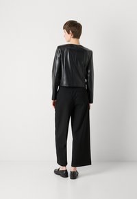 Black leather jacket with a fitted design, cropped length, and smooth texture. Paired with wide-leg trousers in black, featuring a clean cut.