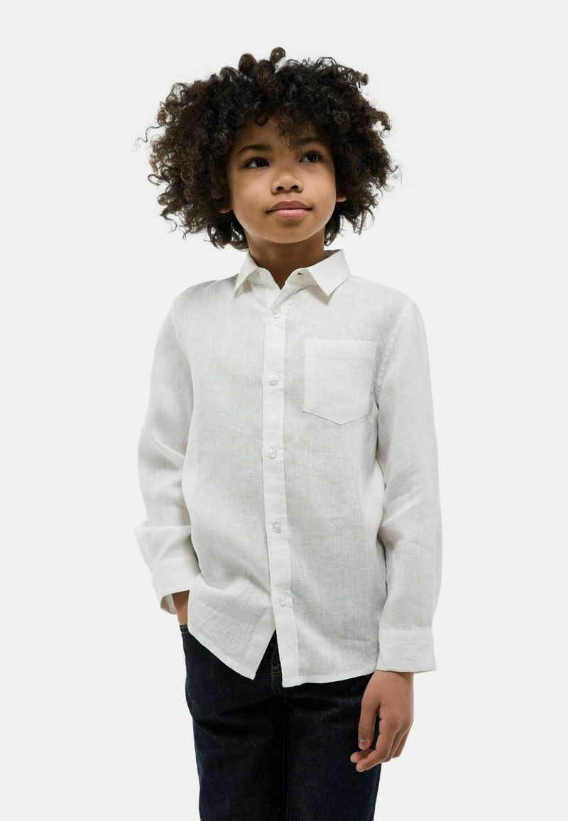 Chemise blanche à boutons en tissu léger, dotée d'une poche poitrine, de manches longues et d'un col classique, associée à un jean foncé.