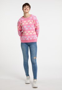 Maglione rosa a maglia con cuori pastello, scollatura tonda e orlo a coste. Abbinato a jeans skinny azzurri e sneaker bianche.