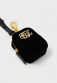 Saco de veludo preto com monograma dourado "BGL", fecho com zíper e uma alça preta destacável com um clip dourado. Forma quadrada compacta.