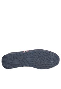 Suela de zapatilla deportiva negra con un dibujo texturizado y patrón, que presenta formas en relieve de zigzag y triángulos, además de franjas de acento rojas y blancas.