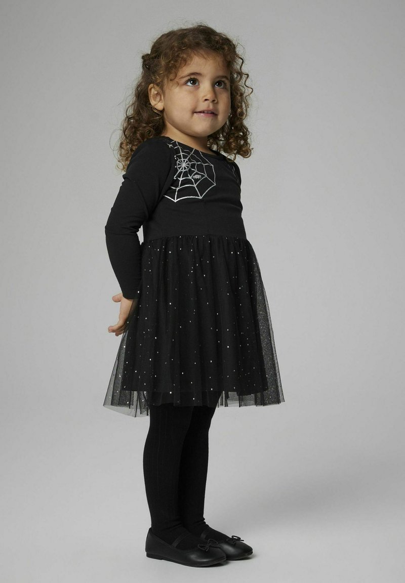 Svart klänning med långa ärmar, med ett silverfärgat spindelnätmönster, tyllkjol med silverstjärnor, tillsammans med svarta leggings och skor.