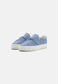 Light blue canvas slip-on sneakers with a twisted design at the front and white rubber soles, featuring a polka dot pattern inside.