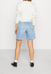 Shorts de mezclilla azul claro con un dobladillo deshilachado y bolsillos traseros, combinados con un sudadera color crema y zapatillas altas negras.