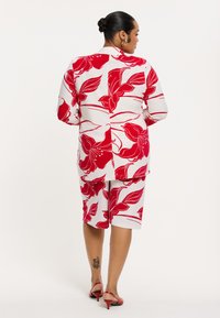 Bloemmotief blouse en shorts set in rood en wit. De stof is zacht, met een comfortabele pasvorm en korte mouwen. Verfraaid met een achternaad.