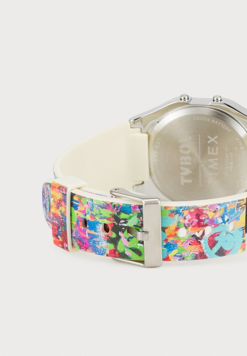 El reloj cuenta con una correa de patrón colorido en tonos de rosa, azul y verde, combinada con una caja de metal plateado y una pulsera de silicona color crema.