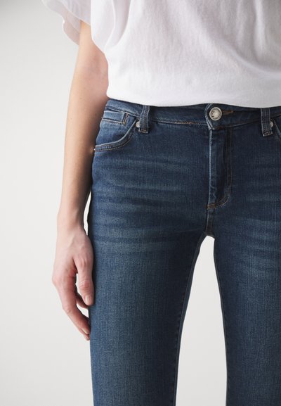 Kék farmernadrág függőleges szabással, elülső gomb- és cipzárzárral, öt zsebbel és finom kopásos részletekkel.