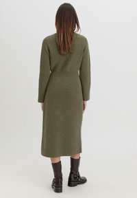 Grünes gestricktes Midi-Kleid mit langen Ärmeln, gerippter Textur, tailliertem Schnitt und gerader Rockform. Kombiniert mit braunen kniehohen Stiefeln.