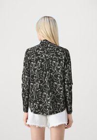 Long-sleeve shirt in black fabric featuring a white abstract face pattern, with a pointed collar and loose fit, worn with white shorts.