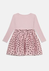Top a maniche lunghe rosa a coste con gonna attaccata, caratterizzata da un sovrapposto trasparente rosa punteggiato di cuori neri, posata su uno sfondo bianco.