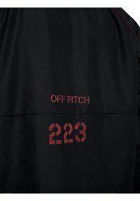 Tissu noir avec texte rouge « OFF PITCH » au-dessus du numéro « 223 » imprimé en police pochoir en gras.
