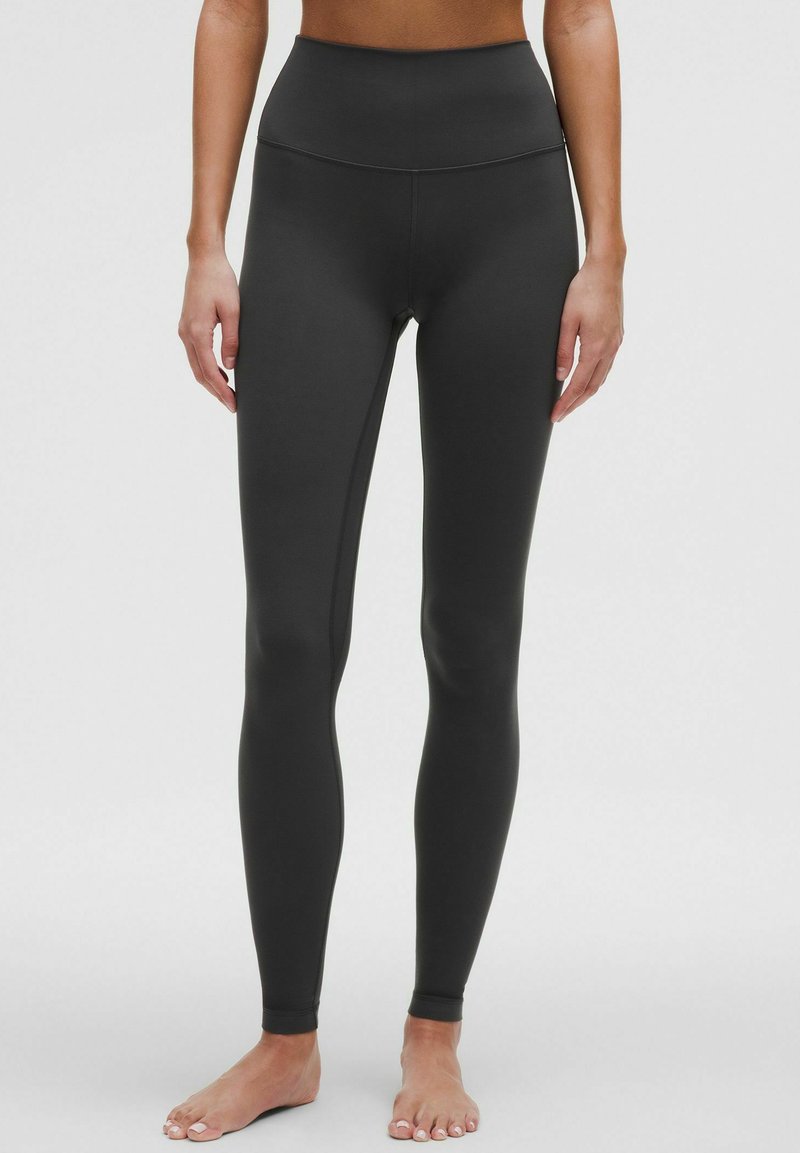 Mustat korkeavyötäröiset leggingsit, jotka on valmistettu sileästä materiaalista. Muotoon liittyvä malli ilman näkyviä kuvioita tai varusteita, jotka ulottuvat nilkkoihin.
