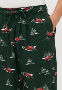 Zöld pizsamán nadrág, állítható derekkal, piros autók és hóval borított fák mintázatával. Puha, könnyű anyagból készült.