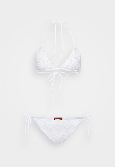 Bela bikinijska sestava z trikotnim zgornjim delom in nastavljivimi vezavami, okrašena z zigzag vzorcem in mehko teksturo. Vključuje usklajene hlačke.