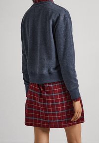 Felpa blu navy con polsini a coste, abbinata a una gonna scozzese rossa con linee bianche e blu, creando un look a strati.