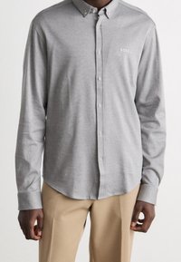 Grijze button-up shirt met een subtiele textuur en geborduurd logo. Heeft een spread collar en lange mouwen, gecombineerd met beige broek.