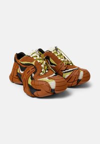 Zapatillas de punto que presentan una combinación de colores marrón, amarillo y negro. Suelas de goma gruesa con acentos texturizados y cordones elásticos.