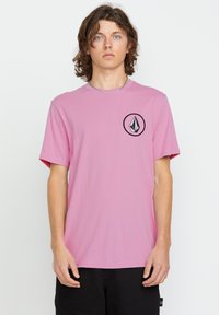 Light pink short-sleeve t-shirt with a round black logo on the left chest. Soft fabric and a relaxed fit. No patterns or accents visible.
