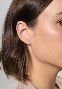 Srebrne kolczyki z pięcioma małymi, okrągłymi, przezroczystymi kamieniami w przesuniętym wzorze, odbijające światło dzięki polerowanemu wykończeniu, noszone na płatku ucha.