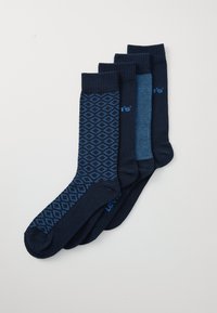 Fire par sokker i marineblå og blå nuancer. Ét par har et geometrisk mønster, mens de andre er ensfarvede eller teksturerede med ribbede manchetter.