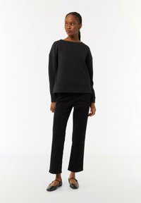 Schwarzes, gesteppte Sweatshirt mit weitem Rundhalsausschnitt, kombiniert mit schwarzen, schmalen Hosen und schwarzen flachen Schuhen. Glatte Textur und minimalistisches Design.