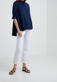 Mörkblå knapplös blus med hög-låg fåll, i kombination med vita raka jeans och svarta sandaletter med remmar. Slätt tyg, avslappnad passform.