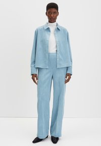 Ensemble en velours côtelé bleu clair comprenant une chemise à boutons avec un col et un pantalon taille haute à rayures verticales. Texture et coupe lisses.