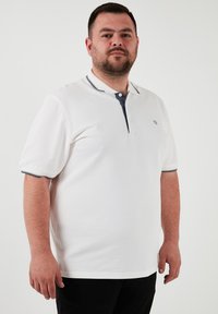 Biela polo košeľa s námorníckym golierom a rade tlačidiel. Má krátke rukávy s námorníckymi akcentmi. Tkanina má textúrovaný povrch.