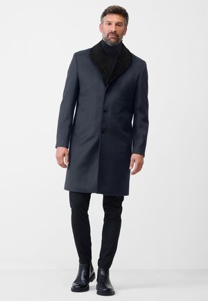 Navy overcoat with a black fur-like collar, single-breasted design, and five buttons, worn over a black turtleneck and black pants.