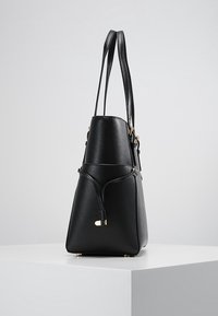 Sac à main structuré noir en matériau synthétique texturé. Dispose de deux longues poignées, d'accents en métal doré et d'un fond effilé.