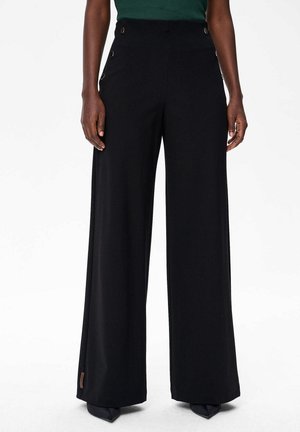 Pantalons larges noirs en tissu lisse, avec une taille haute et des accents de boutons en métal sur le côté, présentant une silhouette ajustée.