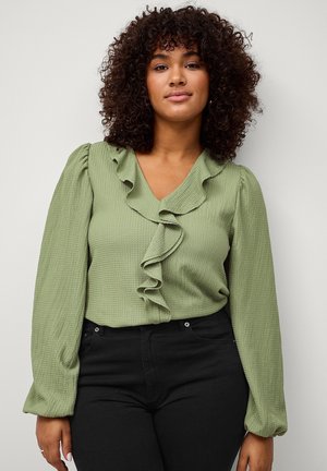 Green textured blouse with ruffled neckline and long puff sleeves, paired with black high-waisted pants.