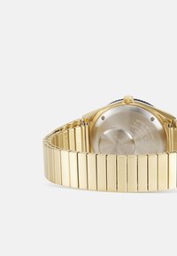 Montre-bracelet en métal doré avec une finition polie, un bracelet à maillons et un boîtier rond. Présente un dos argenté visible et une couronne accentuée de noir.