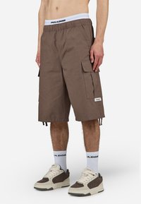 Brune cargo-short med elastisk waistband som har en hvit logo. Inkluderer flere sidelommer og justerbare snorer i kanten.