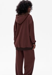 Bruine hoodie met een fluffy kraag, relaxte pasvorm, geribbelde boorden en zoom. Gecombineerd met bijpassende bruine, losse broek. Zachte textuur.