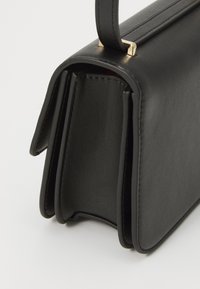 Borsa a mano nera in pelle con un design strutturato, dotata di una tracolla piatta, accessori in metallo dorato e una texture liscia.