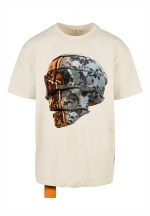 Cremefarvet t-shirt med korte ærmer, der viser et detaljeret kraniumgrafik med prangende blå blomsterdesigns og metalliske accenter.