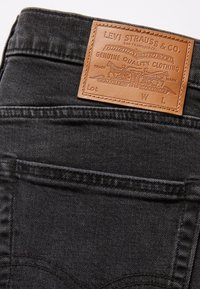 Poche arrière d'un jean en denim noir avec une étiquette en cuir cousue Levi Strauss & Co. affichant la marque et les détails de qualité.