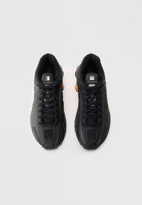 Par črnih Nike Shox superg z oranžnimi detajli, zavezane in prikazane s ptice pogled na enobarvni beli ozadju.