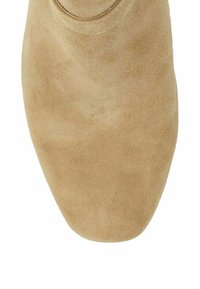 Beige suède schoen met een afgeronde, vierkante neus en zichtbare stiksels nabij de bovenrand.