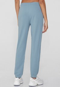 Jasnoniebieskie spodnie dresowe z elastycznym pasem i zwężanymi nogawkami, z gładką fakturą i prążkowanymi mankietami. Buty są białe.