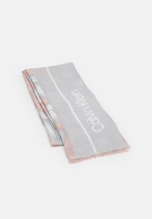Lysegråt foldet tørklæde med sarte lyserøde detaljer og hvid "Calvin Klein" tekst langs den ene kant, med frynsete ender synlige.